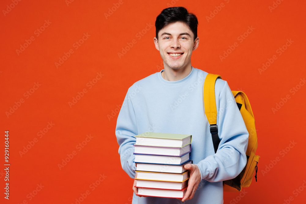 Young smiling smart man student he wears blue casual clothes backpack bag hold in hands stack of books looking camera isolated on plain red orange background. High school university college concept. Young smiling smart man student he wears blue casual clothes backpack bag hold in hands stack of books looking camera isolated on plain red orange background. High school university college concept.
