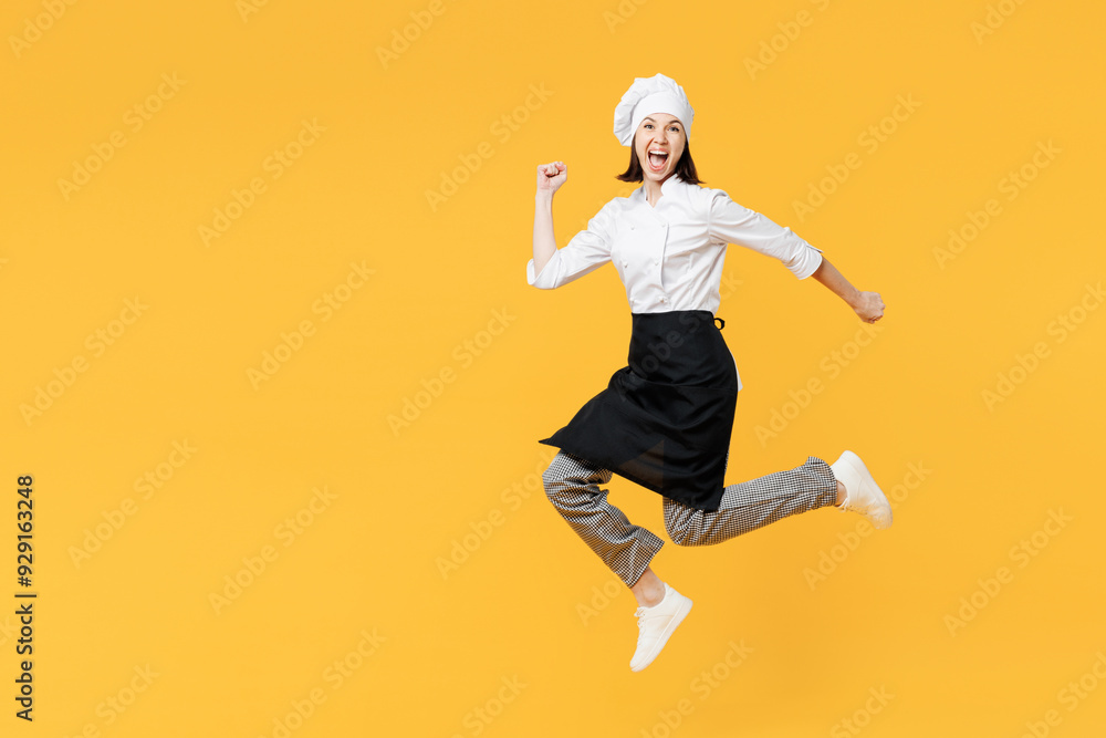 Full body side profile view fun young chef cook baker woman wear white shirt black apron uniform toque hat jump high run fast hurry up isolated on plain yellow background studio. Cooking food concept. Full body side profile view fun young chef cook baker woman wear white shirt black apron uniform toque hat jump high run fast hurry up isolated on plain yellow background studio. Cooking food concept.
