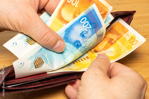 Israel money. Hand taking money out of brown wallet, Israeli shekel banknotes, finance business concept