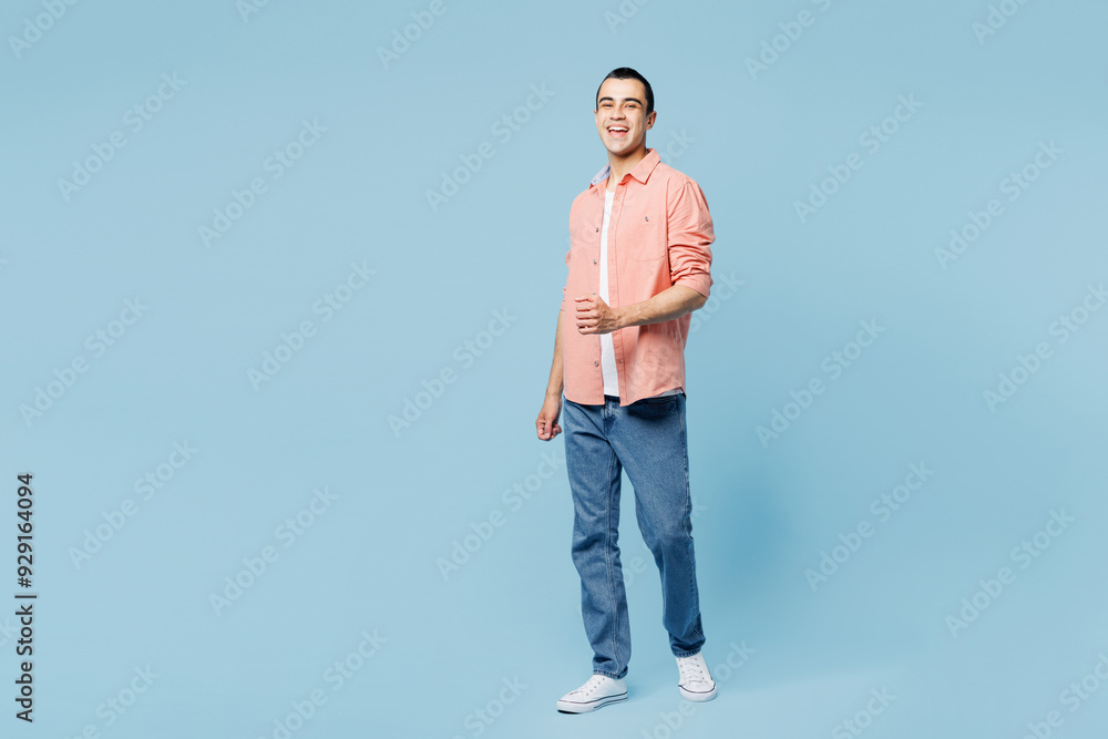 Full body young smiling happy cheerful middle eastern man he wear pink shirt white t-shirt walk go look camera isolated on plain pastel light blue cyan background studio portrait. Lifestyle concept. Full body young smiling happy cheerful middle eastern man he wear pink shirt white t-shirt walk go look camera isolated on plain pastel light blue cyan background studio portrait. Lifestyle concept.