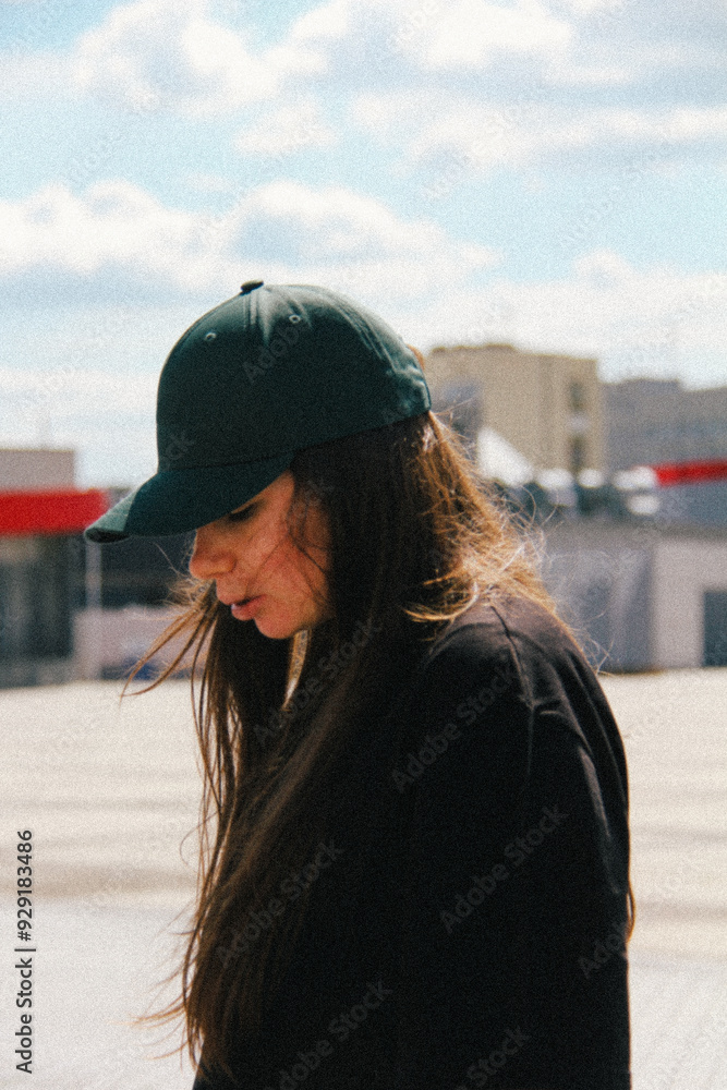 A profile view of a woman wearing a green cap. The light, subtle blur, and graininess focus attention on her relaxed posture, creating a minimalist yet visually compelling image.