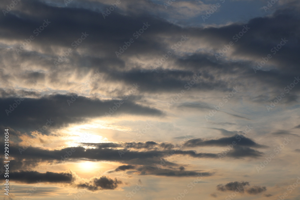 Obraz premium A sunset over the horizon, with delicate shades of gold and grey, as the sun dips below the horizon. Clouds create serenity and drama to the scene.