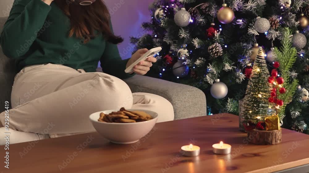 A woman drinking coffee and shopping on her phone. Christmas tree and atmosphere in the background. Preparing for New Year and Christmas. Wrapping Christmas presents A woman drinking coffee and shopping on her phone. Christmas tree and atmosphere in the background. Preparing for New Year and Christmas. Wrapping Christmas presents