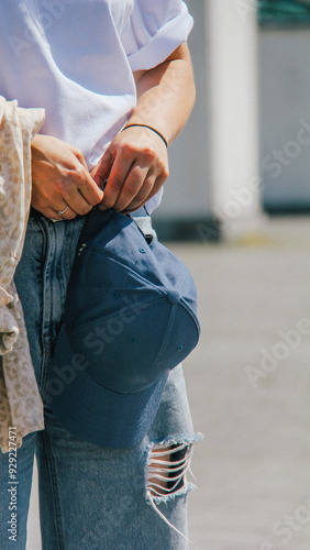 Obraz na płótnie Close-up of a woman holding a blue cap paired with ripped blue jeans. The casual and laid-back style emphasizes modern urban fashion trends. w salonie