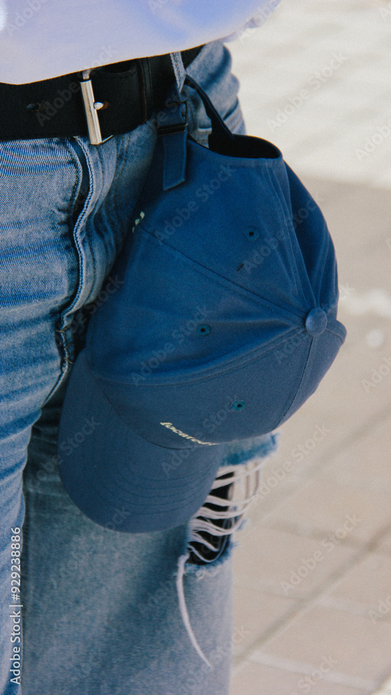 Detailed shot of blue denim jeans with a blue cap hanging from the belt loop. The cap has Mariupol printed on it, translating to