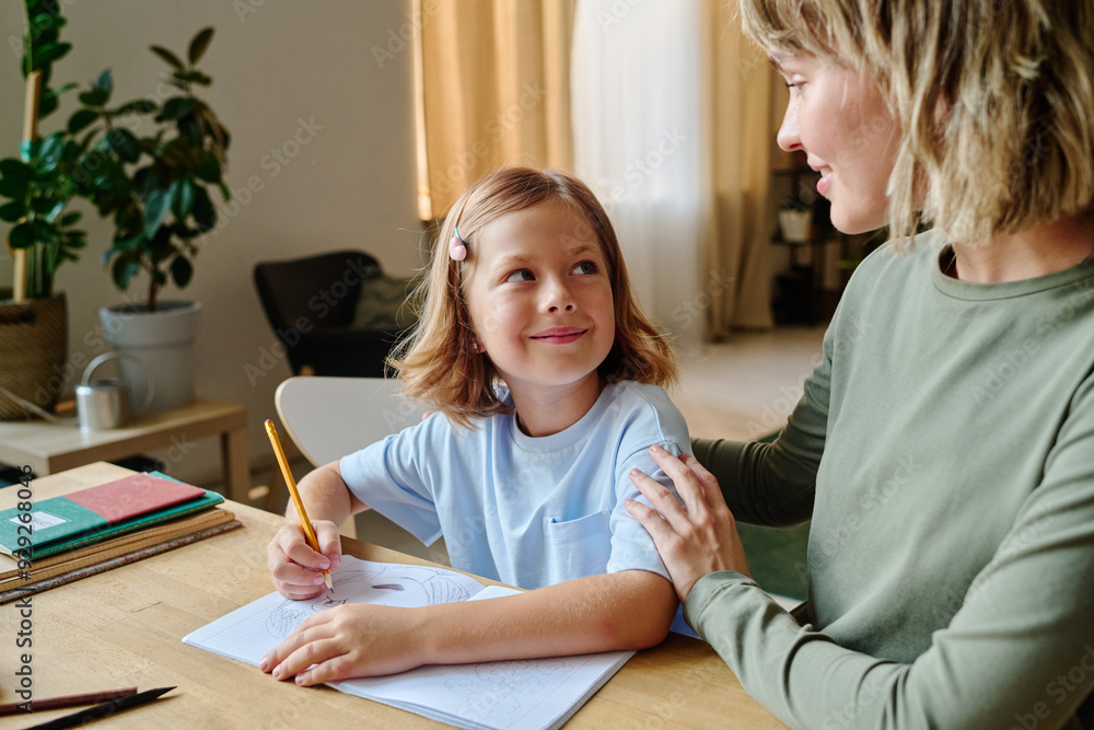 Smiling girl looking at her blonde mother while they sitting at table Smiling girl looking at her blonde mother while they sitting at table