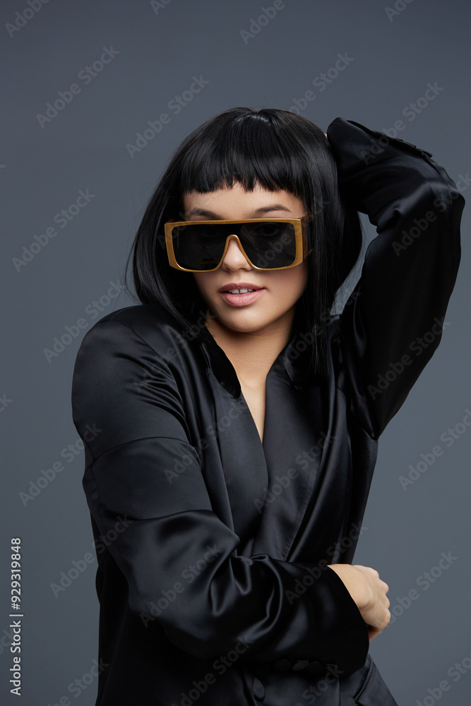 Woman in sunglasses and black blazer poses with hands on hips against gray background, exuding confidence and style Woman in sunglasses and black blazer poses with hands on hips against gray background, exuding confidence and style