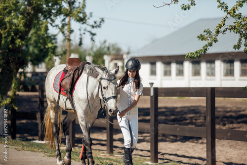 A young equestrian is gently guiding a beautiful white horse in a sunny, charming stable