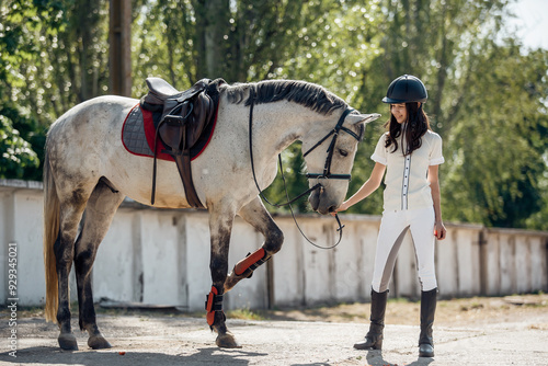 A young equestrian is gently guiding a beautiful white horse in a sunny, charming stable