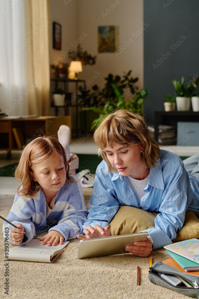 Mom and her kid studying together on floor, mother showing examples via tablet Mom and her kid studying together on floor, mother showing examples via tablet