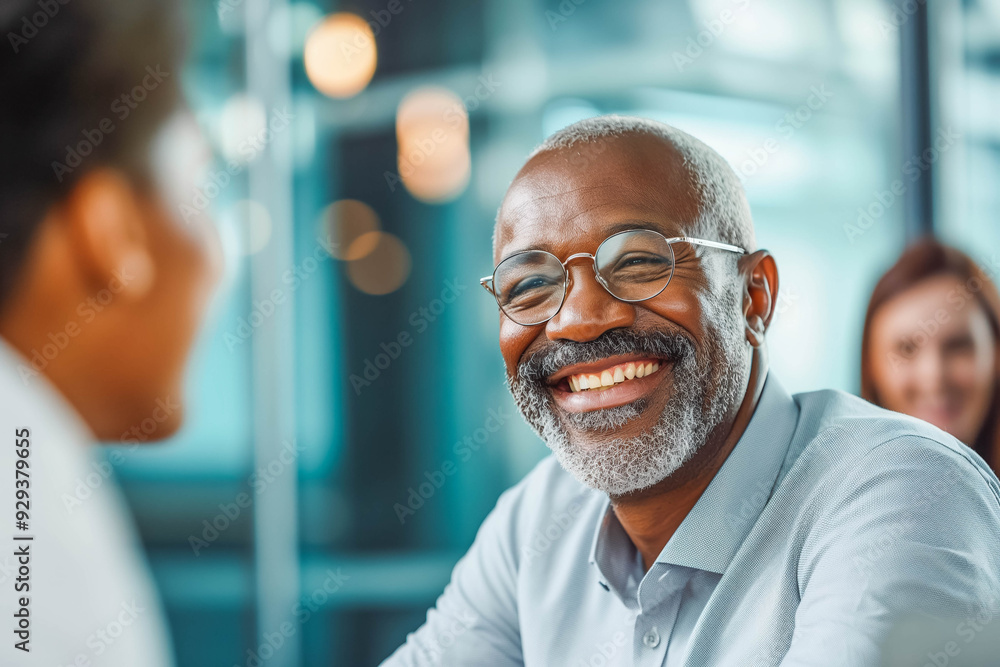 © MVProductions - A mature businessman smiles warmly during a meeting with a younger colleague, sharing his expertise and experience in a modern office setting. © MVProductions - A mature businessman smiles warmly during a meeting with a younger colleague, sharing his expertise and experience in a modern office setting.