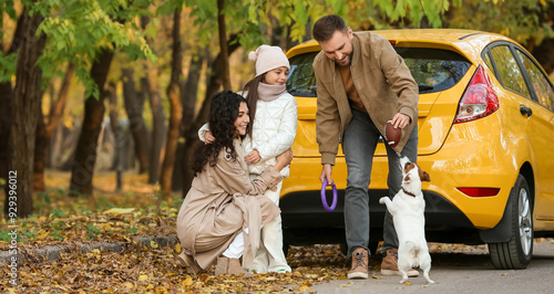 Happy family playing with cute dog near yellow car on autumn day