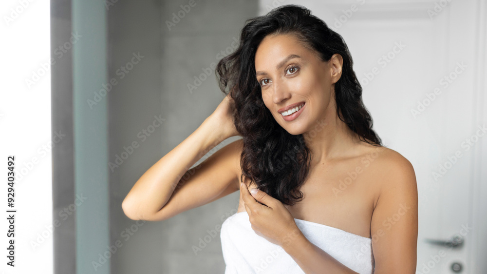 Natural beauty and morning skincare routine. Happy lady touching her curly hair and smiling at her reflection in mirror in bathroom Natural beauty and morning skincare routine. Happy lady touching her curly hair and smiling at her reflection in mirror in bathroom