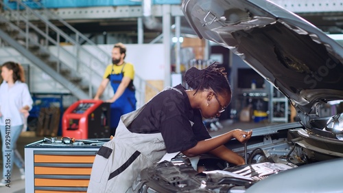 African american mechanic in garage using torque wrench to tighten bolts inside opened up vehicle, preparing to change oil. Auto repair shop expert doing checkup on car to prevent issues