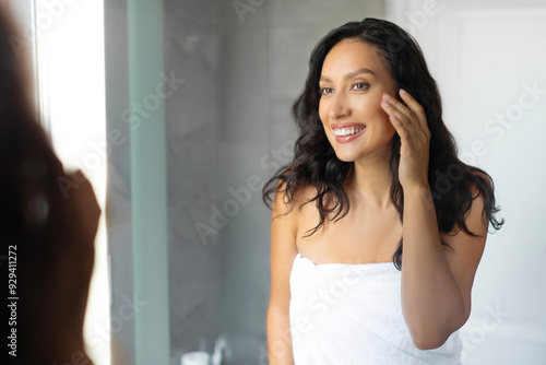 Happy young European woman touching her face while looking at reflection in mirror, pampering herself after morning shower Free Download Happy young European woman touching her face while looking at reflection in mirror, pampering herself after morning shower - GFXLoad