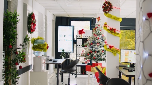 Tilt up shot of empty festive ornate modern office workspace with beautiful Christmas tree and lights. Xmas adorn workplace ready for festivities before winter holiday season vacation