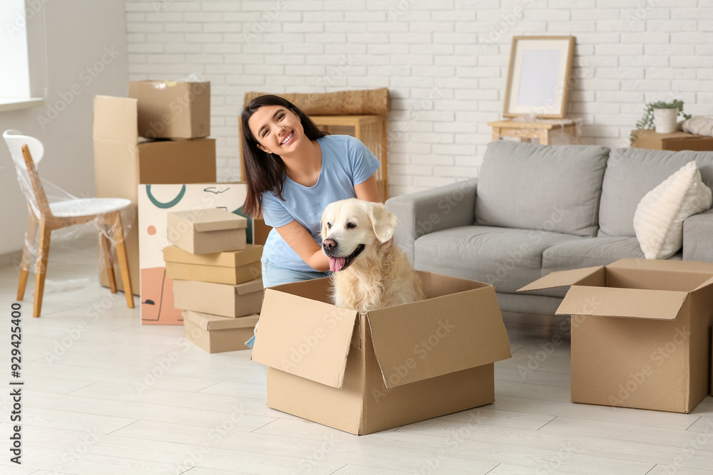 Fototapeta premium Young happy woman and cute Labrador dog with boxes on moving day sitting at home