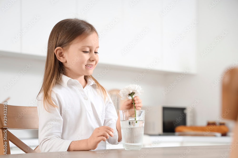 Cute little girl putting flower into glass of water in kitchen Cute little girl putting flower into glass of water in kitchen