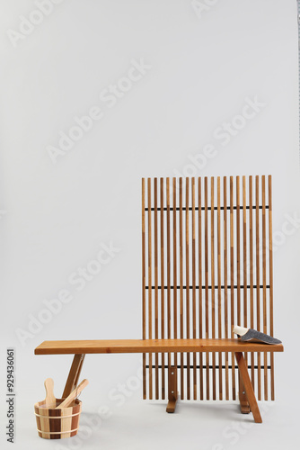 Wooden bench with massage glove, bucket and folding screen on light background