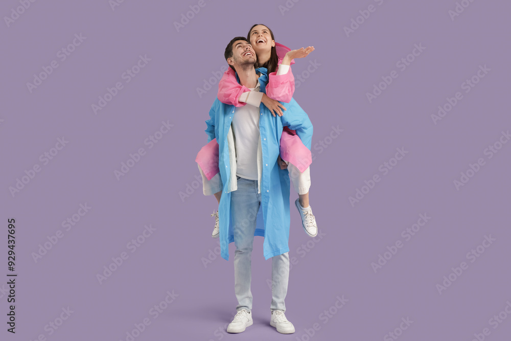 Young couple in raincoats on lilac background Young couple in raincoats on lilac background