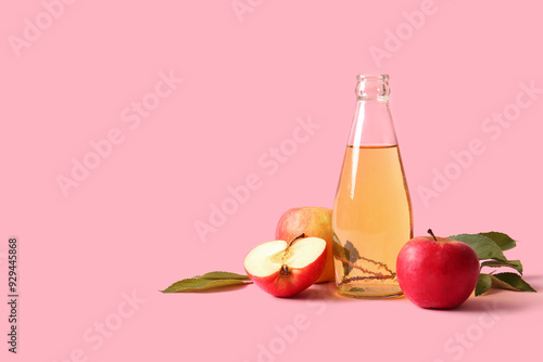 Bottle of fresh apple cider and fruits on pink background