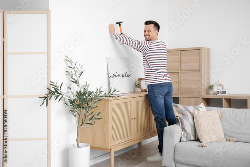 Fotografija Young man hammering nail into wall for poster at home