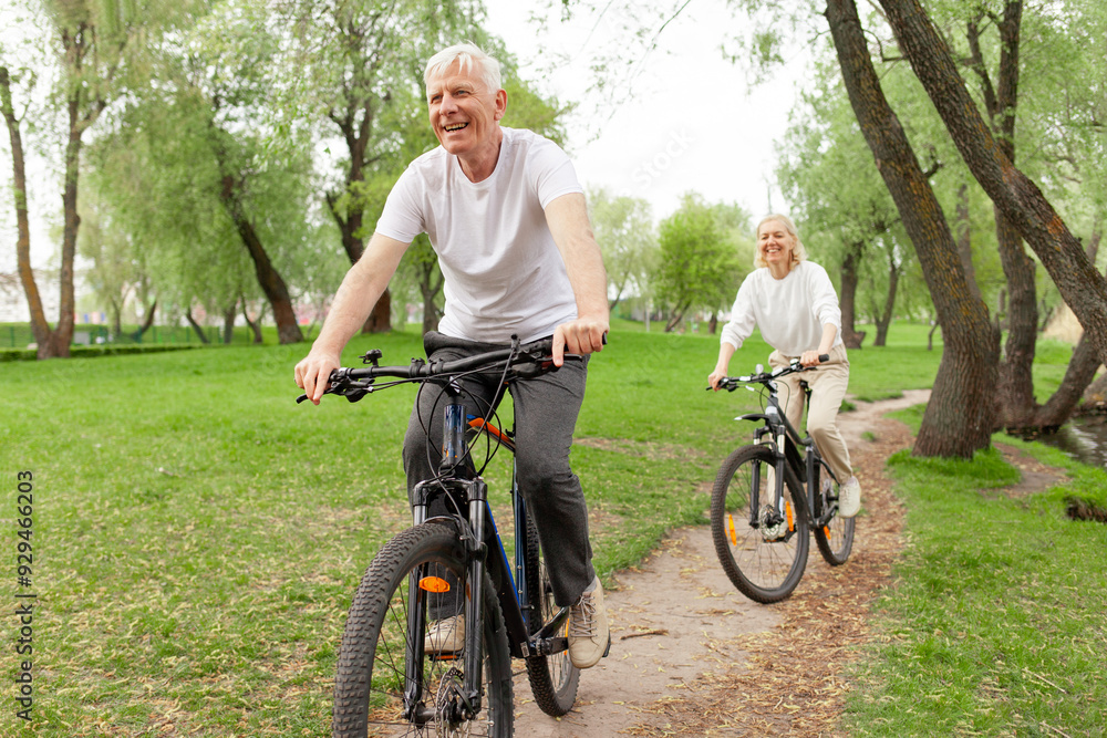 Obraz premium elderly senior couple rides bicycle in the park in the summer and smiles, old gray-haired man and woman are actively resting outdoors, old people practice cycling in forest