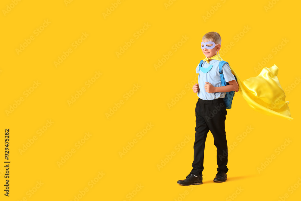 Happy schoolboy dressed as superhero blackboard with backpack on yellow background Happy schoolboy dressed as superhero blackboard with backpack on yellow background