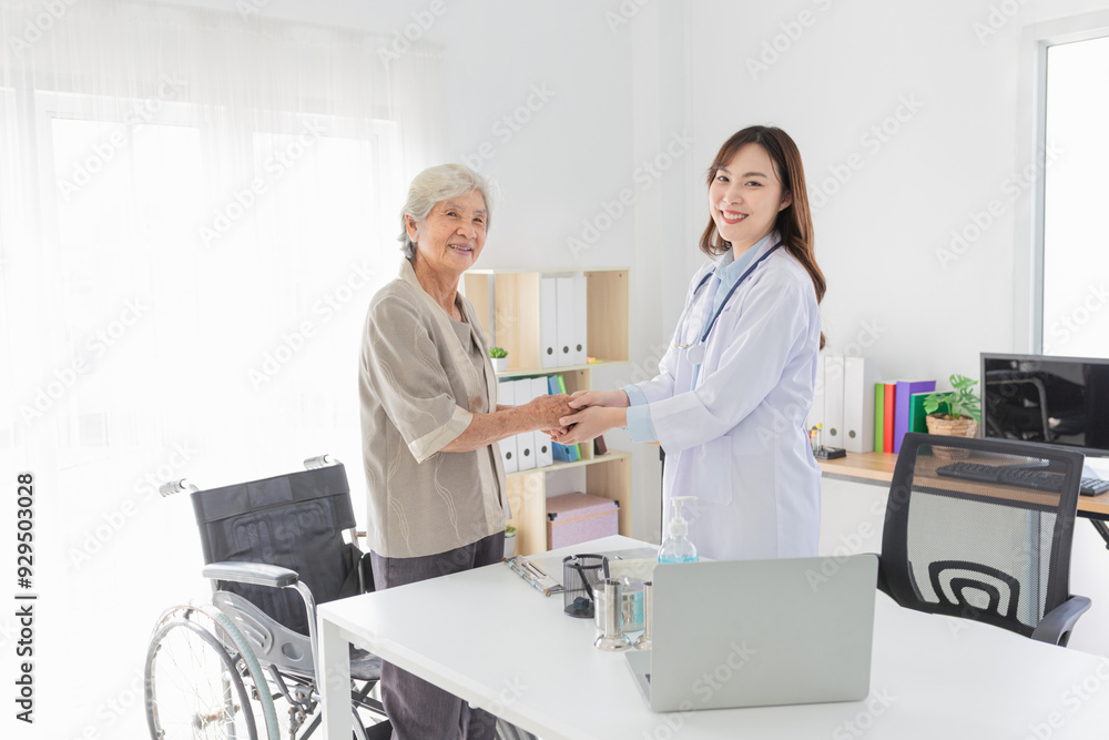 Obraz premium Asian female doctor warmly greeting elderly patient in medical office. They holding hand together, geriatric care, and positive doctor-patient relationship in a clinical setting.