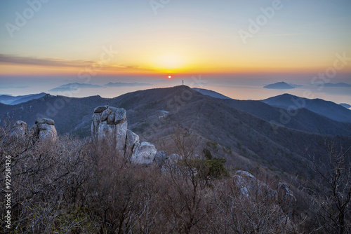 Namhae-gun, Gyeongsangnam-do, South Korea - April 5, 2022: Sunrise view of rocks and trees on Geumsan Mountain against islands and rising sun on the sea in early spring photo