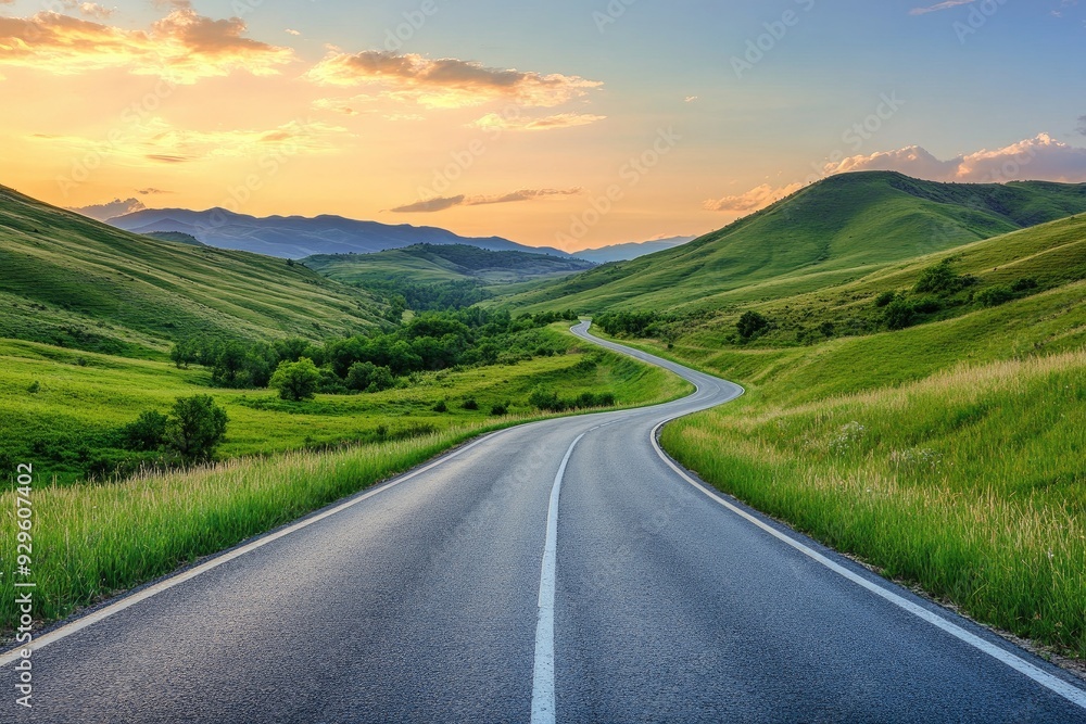 Naklejka premium Serene winding road through lush green hills under a colorful sunset sky, perfect for nature and travel photography.