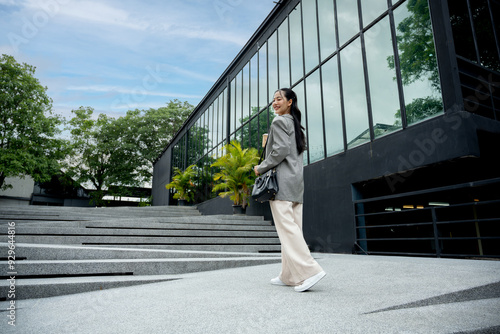 A young woman is walking down the stairs in front of a large glass building.