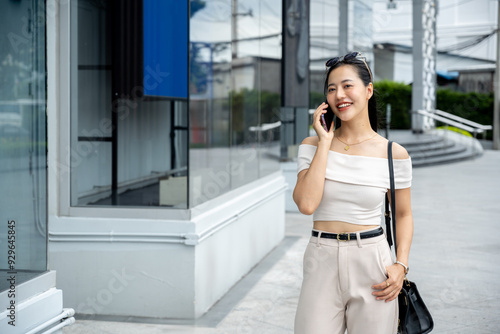 A young woman is standing on the sidewalk in front of a building, talking on her phone