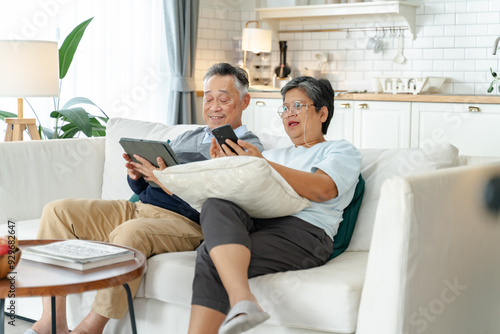Senior Asian couple grandparents using a smart phone together on sofa at home.Senior asian elderly couple enjoy retirement life at home.happiness retirement,Healthcare,Asian happy family concept
