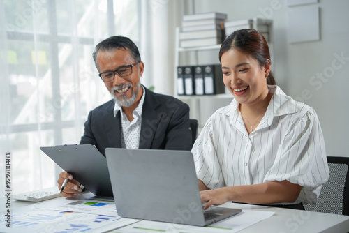 Two business partners, a man and a woman, are analyzing data and working together on a laptop in their office