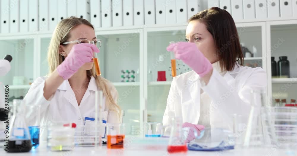 Two scientists examine orange liquid samples in test tubes in laboratory setting Two scientists examine orange liquid samples in test tubes in laboratory setting