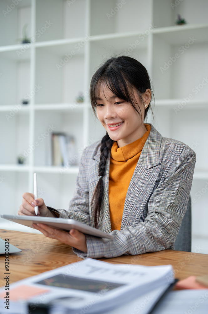 A charming, positive Asian businesswoman is using a digital tablet at her desk in the office. A charming, positive Asian businesswoman is using a digital tablet at her desk in the office.