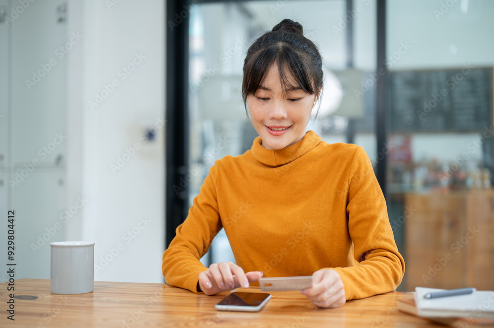 A beautiful Asian woman holding a credit card and using her smartphone, paying bills online. A beautiful Asian woman holding a credit card and using her smartphone, paying bills online.
