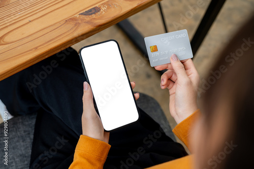 A close-up top view image of a woman sits at a table, holding a credit card and her smartphone. photo