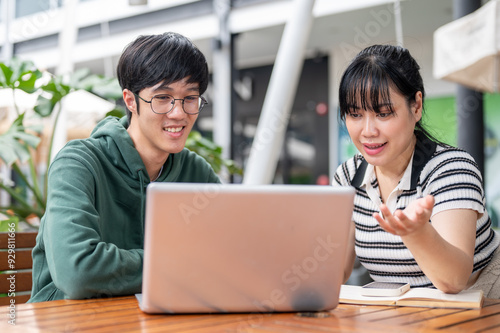 Two young Asian college students are discussing work and doing on a co-project together.