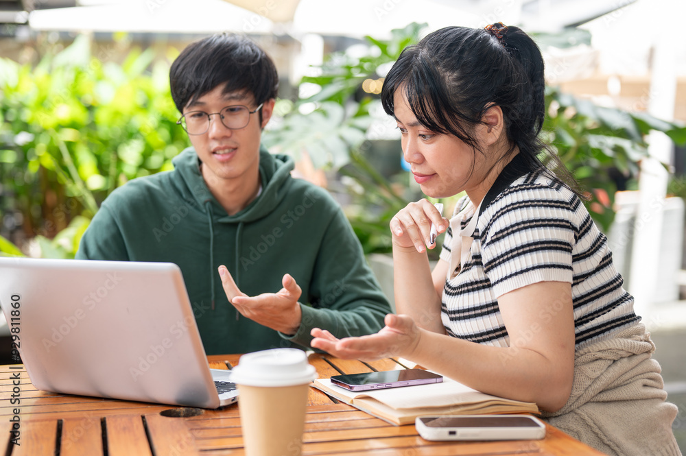 A positive Asian woman is working on a co-project with her friend, showing something on her laptop. A positive Asian woman is working on a co-project with her friend, showing something on her laptop.
