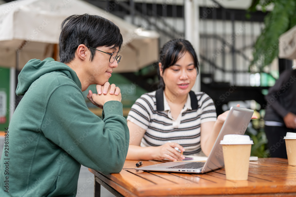 A man looking at a laptop screen and focusing on listening to his friend while she explains work A man looking at a laptop screen and focusing on listening to his friend while she explains work