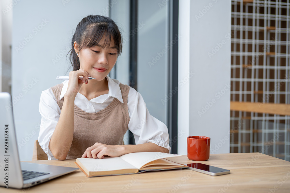 A beautiful, positive Asian woman writing in a book, working at a desk indoors, doing homework. A beautiful, positive Asian woman writing in a book, working at a desk indoors, doing homework.