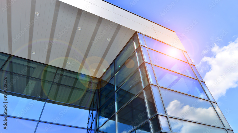 Obraz premium Fragment of a modern building made of steel and glass. Abstract modern commercial architecture fragment. Walls made of shiny glass and steel under blue sky.