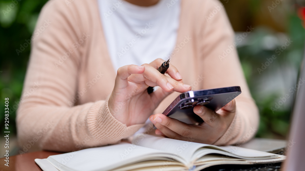 Fototapeta premium A close-up image of a woman using her smartphone while holding a pen, browsing the internet.