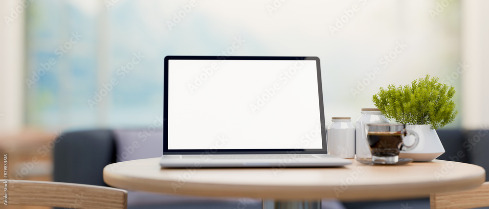 A laptop computer with a white-screen mockup on a round wooden table in a minimalist cafe. A laptop computer with a white-screen mockup on a round wooden table in a minimalist cafe.