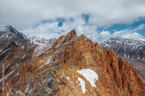 Vivid sharp pinnacle in sunlight. Shiny pointy peak of gold color. Colorful red rocky peaked top. Freshly fallen snow in high mountains. Sunny cloudy alpine view. Snowy cornice on stony mountain ridge photo