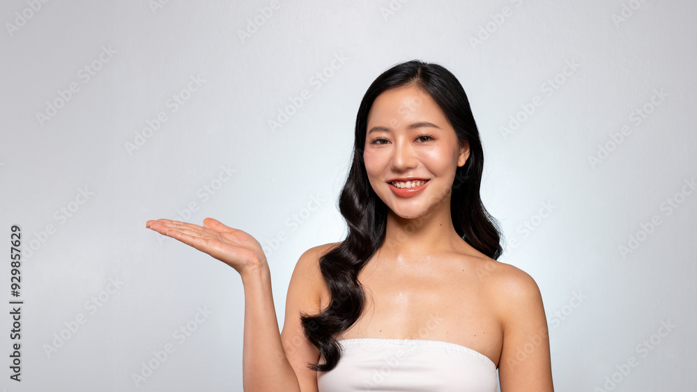 An Asian beauty model poses with her palm open against a grey background, smiling at the camera. An Asian beauty model poses with her palm open against a grey background, smiling at the camera.