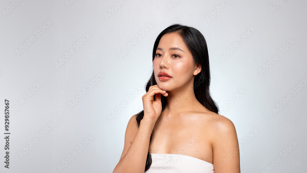 Gorgeous Asian woman with a beautiful face poses against a grey background, gently touching her chin Gorgeous Asian woman with a beautiful face poses against a grey background, gently touching her chin