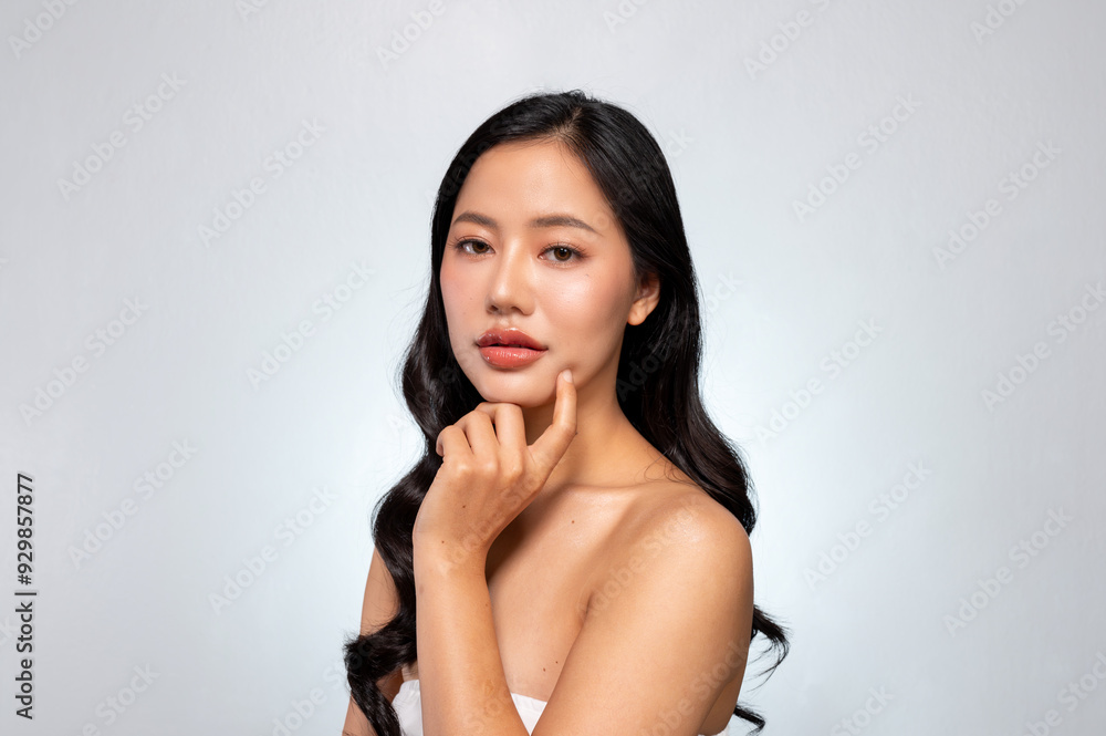 Gorgeous Asian woman with a beautiful face poses against a grey background, gently touching her chin Gorgeous Asian woman with a beautiful face poses against a grey background, gently touching her chin